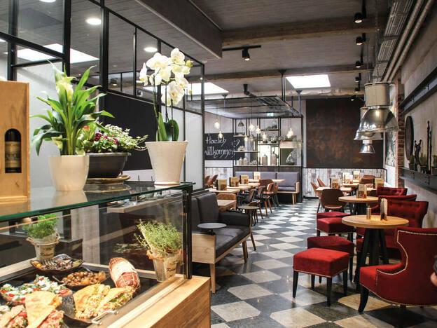 Modernes Restaurant-Interieur Stilvoller Gastronomie Ladenbau mit schwarz-weiß kariertem Boden, gemütlichen Sitzbereichen und einer beleuchteten Vitrine.