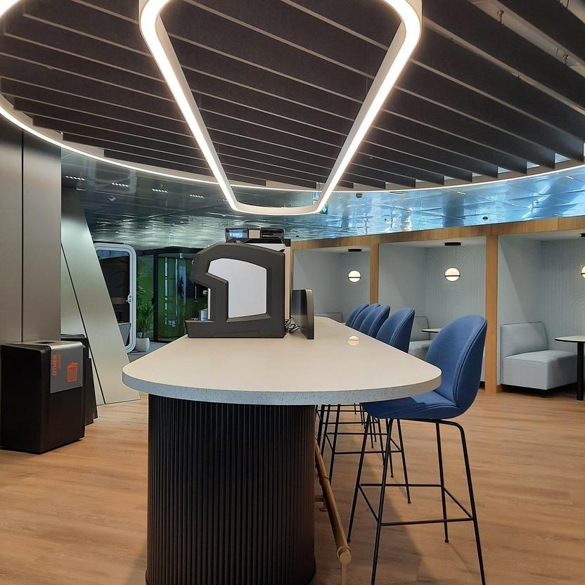 Moderne Büroküche mit einzigartiger Deckenbeleuchtung, runder Bar und blauen Stühlen.