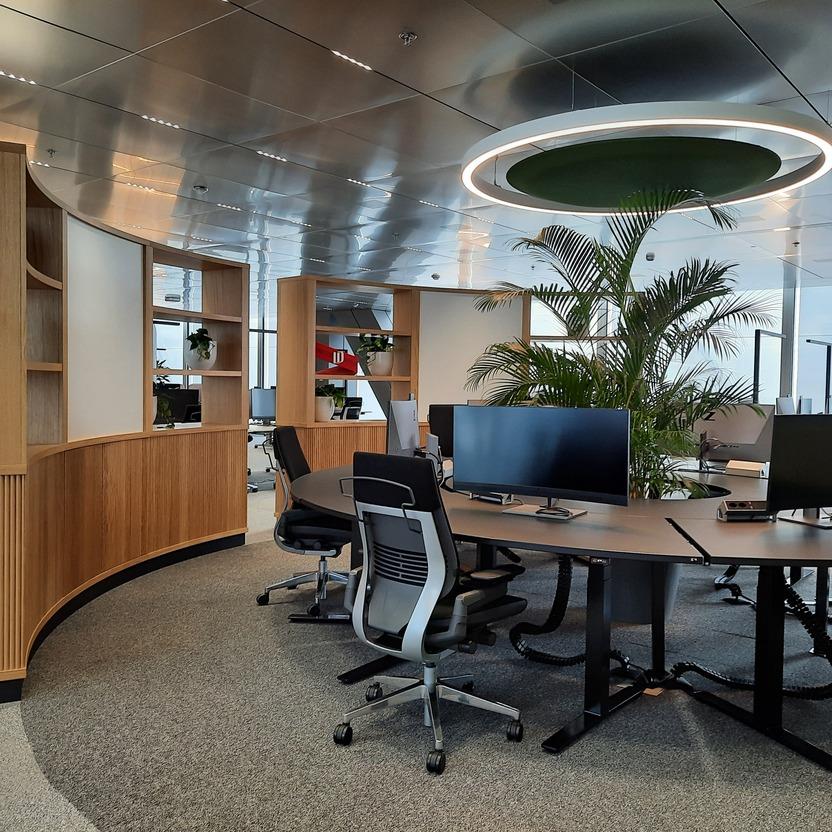 Offener Bürobereich mit Holzregalen, Schreibtischen, Computern und zentraler Ringbeleuchtung.