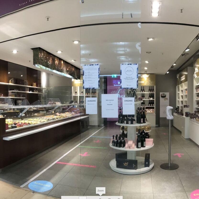 Innenansicht einer Confiserie mit Schokoladen- und Weinregalen und Wegweisern für Ein- und Ausgang.