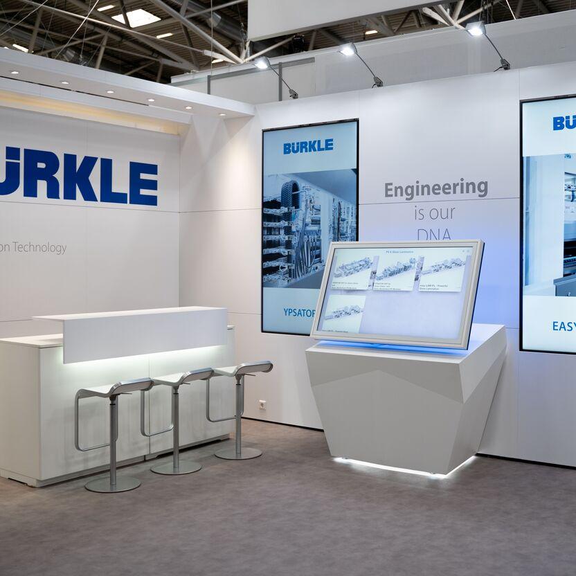 Professionell gestalteter Messestand von Bürkle mit Informationsdisplays und einem Empfangstresen.