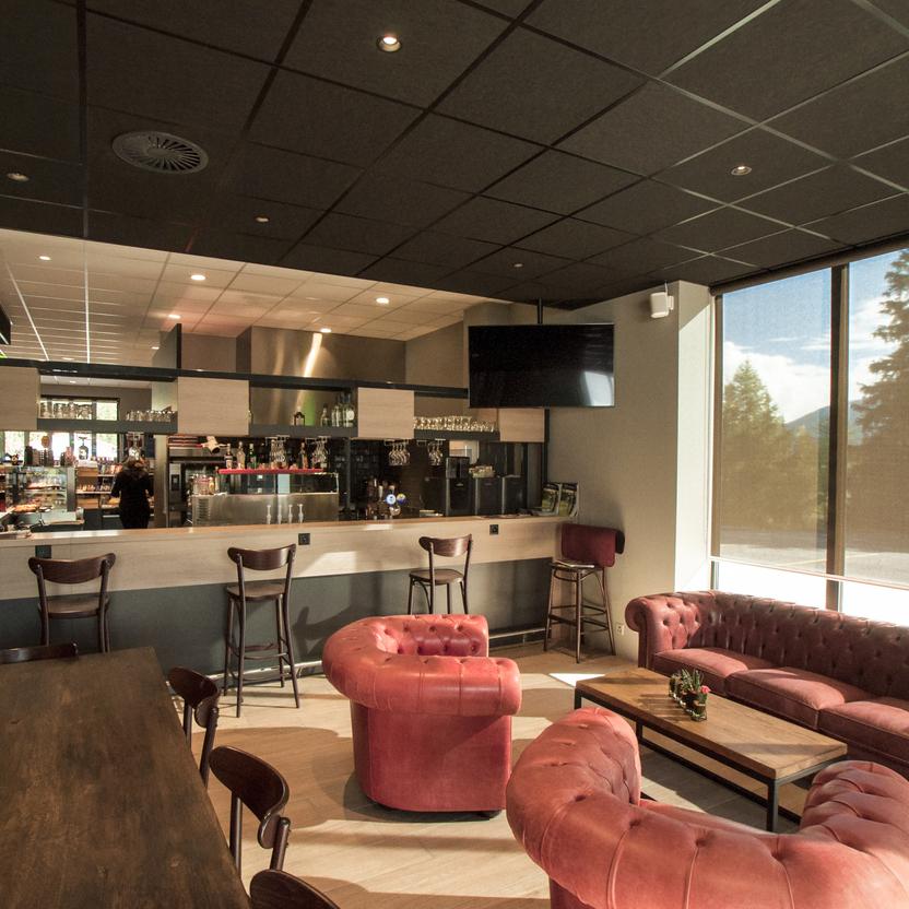 Einladendes Café mit dunklen Decken, roten Chesterfield-Sofas und Barhockern vor großen Fenstern