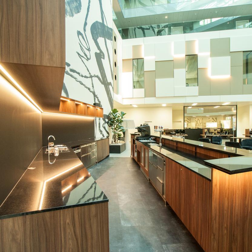 Helles Atrium eines Hotels mit stilvoller Küche, beleuchteten Paneelen und Sitzgelegenheiten.