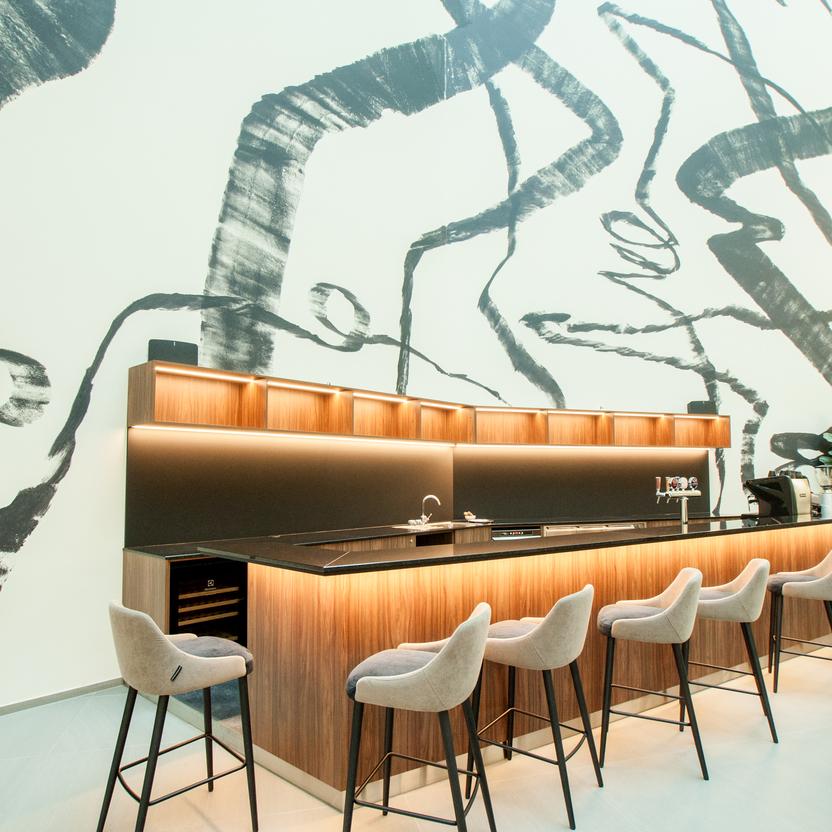 Helle Bar mit stilvollen Barhockern und einer großen abstrakten Kunstwand im Hintergrund.