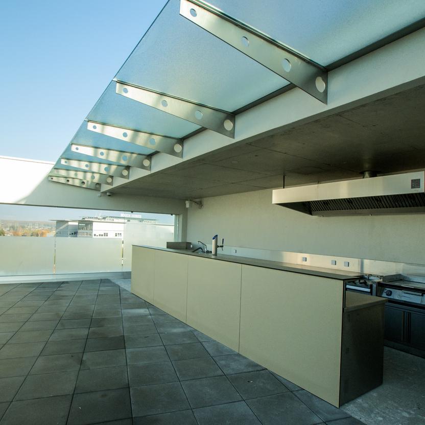 Moderne Außenküche auf einer Dachterrasse mit urbaner Aussicht und futuristischer Überdachung.
