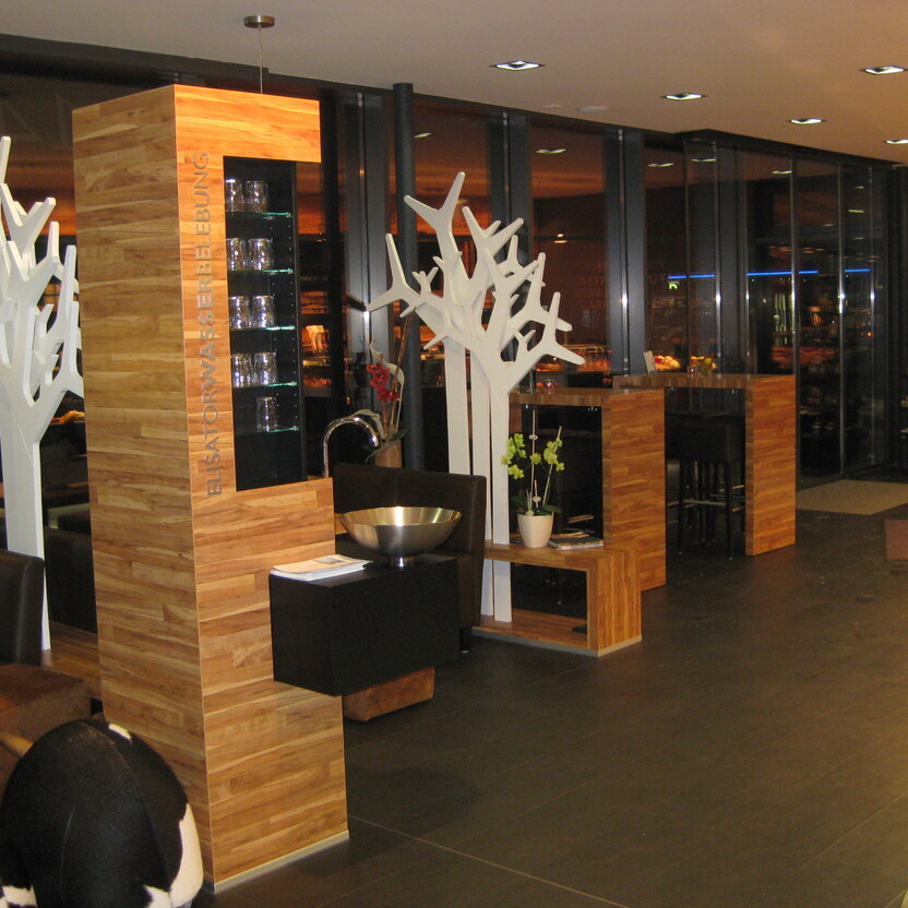 Eleganter Gastronomie Ladenbau mit Holzelementen, dekorativen weißen Baumskulpturen und moderner Beleuchtung.