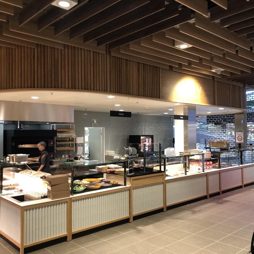 Moderne Frontcooking-Theke mit Grillbereich, Salatbar und offener Deckengestaltung im strukturierten Ladenbau