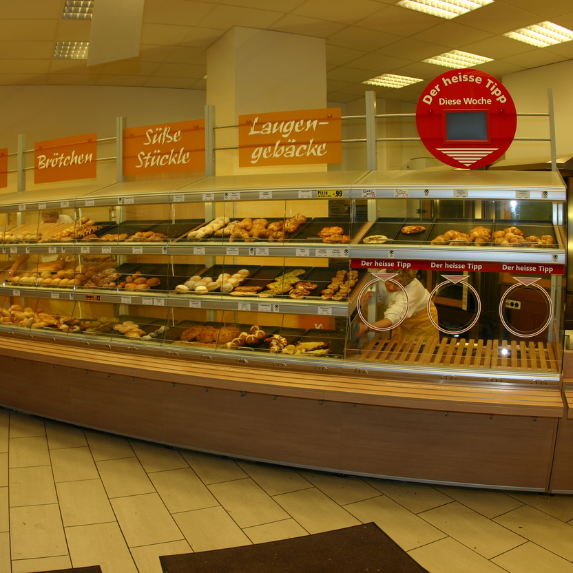 Übersichtliche Bäckereitheke mit Selbstbedienung, Brotregalen und Hinweisschild im modernen Ladenbau