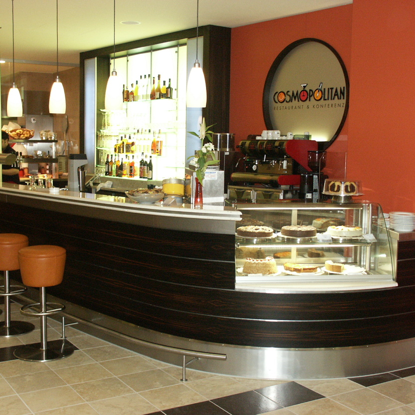 Gepolsterte Barhocker, geschwungene Theke und Kuchenvitrine im eleganten Ladenbau mit Barambiente