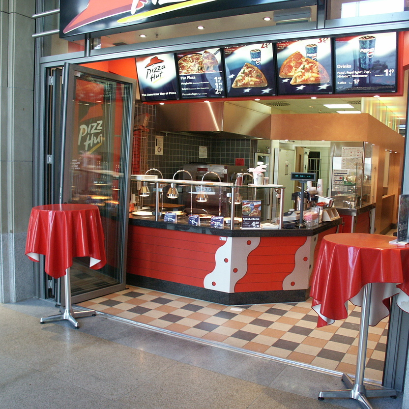 Offene Pizza-Theke mit Menüanzeigen, rot verkleideter Front und funktionalem Ladenbau im Durchgang