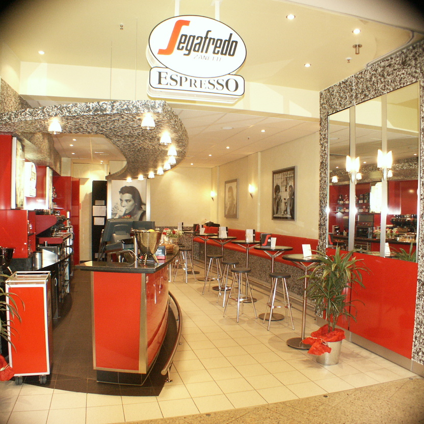 Espresso-Bar mit Sitzplätzen, geschwungener Decke und klar strukturiertem Ladenbau im Centerbereich