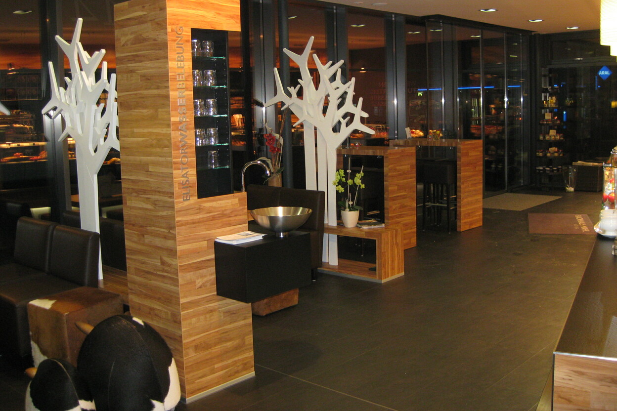 Eleganter Gastronomie Ladenbau mit Holzelementen, dekorativen weißen Baumskulpturen und moderner Beleuchtung.