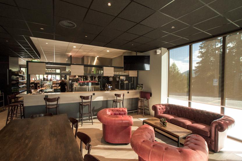 Modernes Café-Interieur Moderner Gastronomie Ladenbau mit eleganten roten Sofas, Barhockern und einer gut ausgestatteten Bar im Hintergrund.