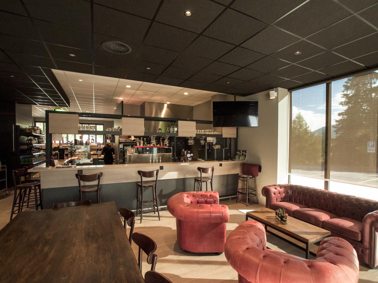 Modernes Café-Interieur Moderner Gastronomie Ladenbau mit eleganten roten Sofas, Barhockern und einer gut ausgestatteten Bar im Hintergrund.