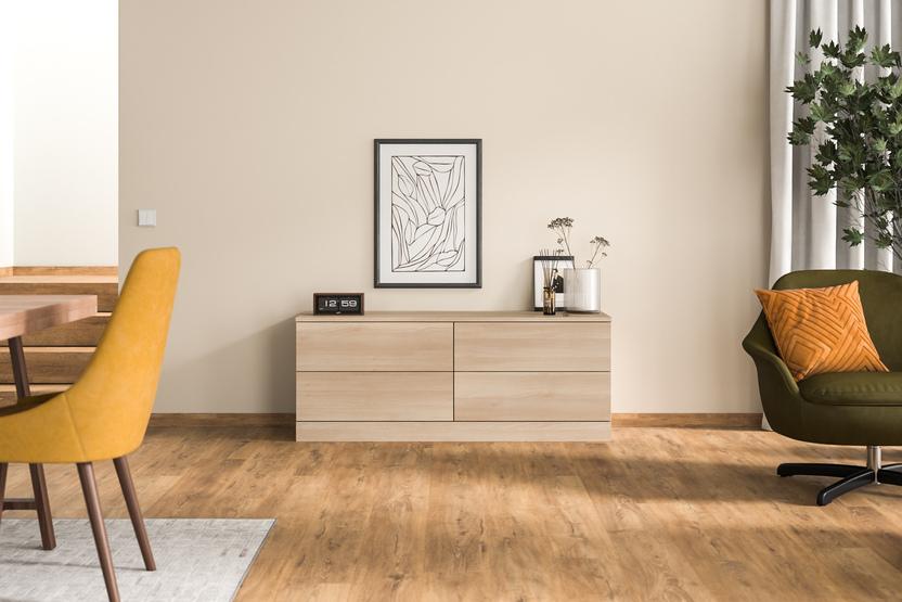 Moderne, ma&szlig;gefertigte Kommode aus hellem Holz vor einer schlichten Wand, neben einem gr&uuml;nen Sessel und unter einem Kunstwerk.